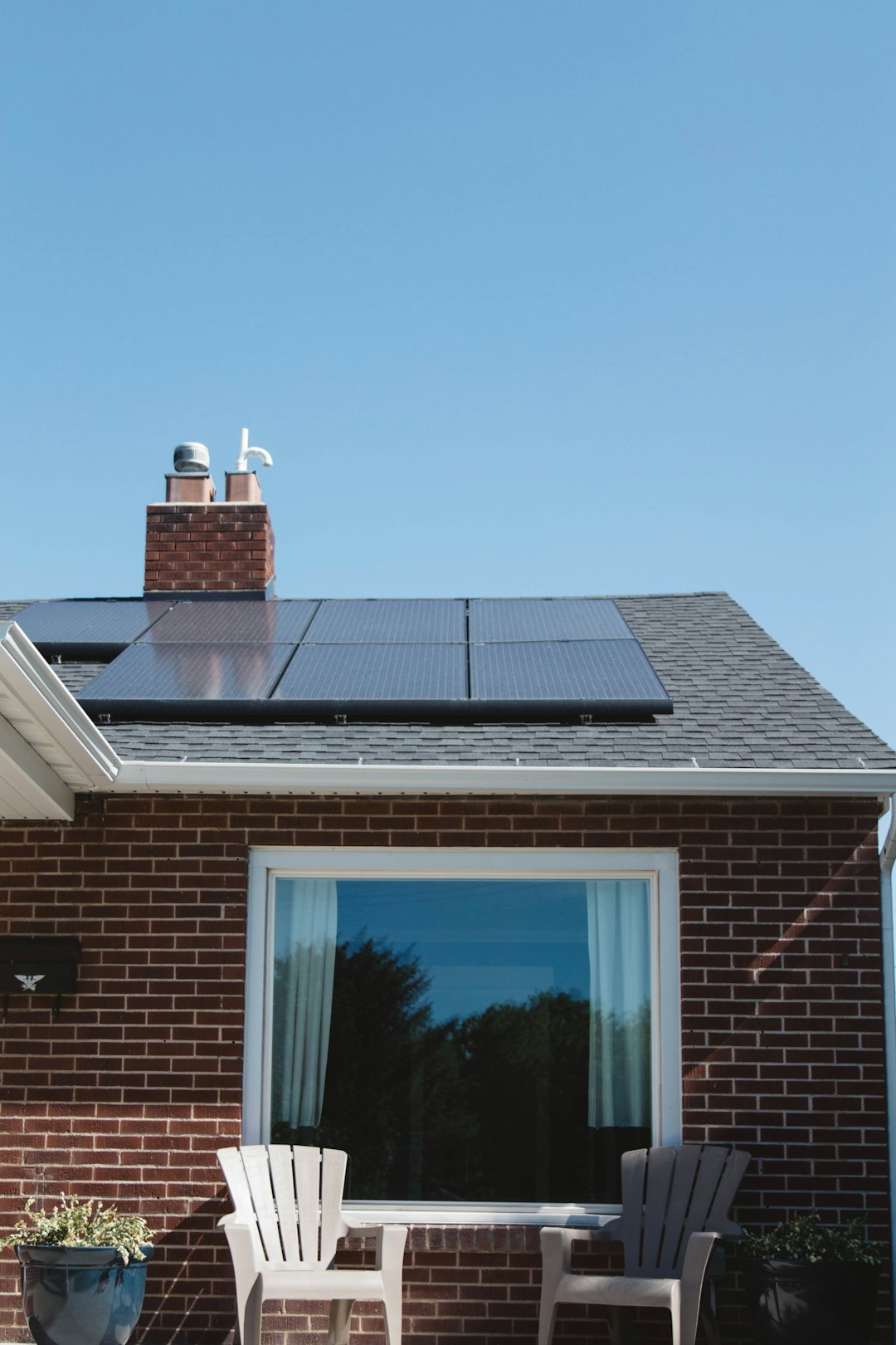 Offerings Vivint Solar - Solar Panels on roof of brick home with window and Adirondack chairs.